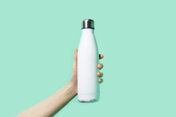 Close-up of female hand, holding white reusable steel stainless eco thermo water bottle on background of cyan, aqua menthe color. Be plastic free. Zero waste.