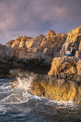 Female sitting on the rock above the sea and working on computer. Business woman working from the beach. Working from distance concept. Freelancer travel and work online.