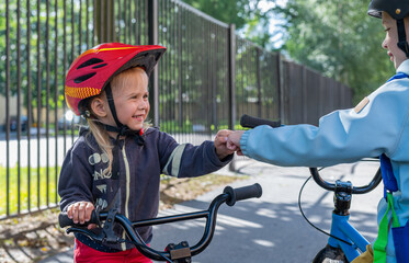 Obraz premium Two children boy and girl greeting each other with fist bump. Friendship, support, equality and diversity. Kids with bicycles are greeting each other on the back yard schools.