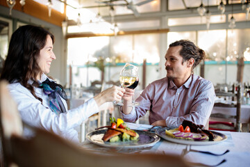 Smiling and happy young couple making a toast and drinking wine, celebrating their anniversary or birthday in a restaurant