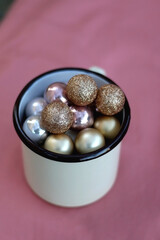 Enamel mug filled with gold baubles. Selective focus, pink background.