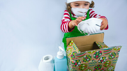 Little elf holding a COVID 19 pandemic present with a sanitizer, medical mask, and toilet paper. Conceptual photo of a gift during corona virus.