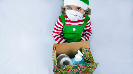Little elf holding a COVID 19 pandemic present with a sanitizer, medical mask, and toilet paper. Conceptual photo of a gift during corona virus.