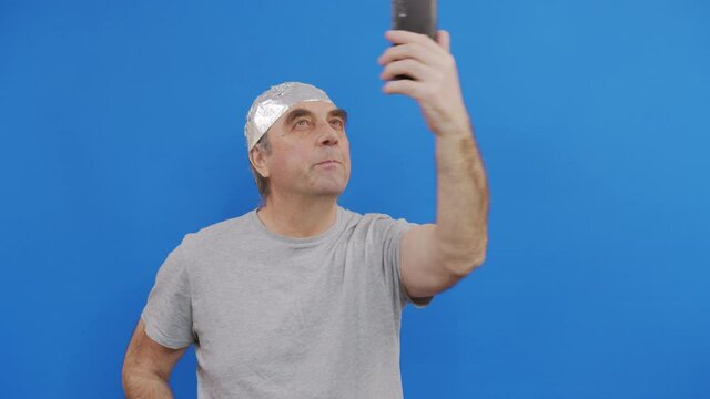 Frightened man in a tinfoil hat waved off the 5G waves.5G tower radiation protection. Irrational fear of a non-existent problem. Protective foil helmet to the brain from aliens.