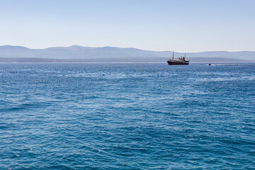 Ein Schiff und kleines Boot am Meer in Kroatien am blauen Wasser mit Bergen im Hintergrund