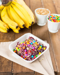 Brazilian Açai on a white Styrofoam box pot with confetti on a wooden background and fruits at...