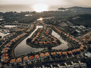 Top view of sunny green city filled with a huge number of trees and houses, in the middle of which there is a lake