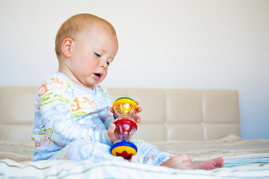 Cute child boy sitting in pajamas on the bed and playing with colored toy.