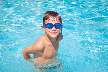 Fototapeta na wymiar Happy boy in a swimming pool. Cute little kid boy having fun in a swimming pool. Outdoors. Sport activities for children.
