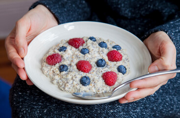 Young woman with bowl of oatmeal and berries.Girl eating breakfast with oatmeal, raspberries, blueberries, chia seeds.Girl holding healthy homemade breakfast. Healthy snack or breakfast in the morning