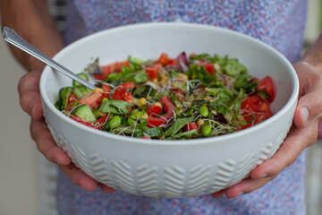 Top view on Female's hands holding a large bowl with a fresh salad. Healthy eating concept. Close-up.