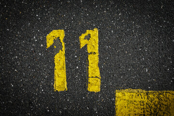 Grey asphalt road, yellow painted number eleven on grey street, yellow lines like a corner on the road, space for text 