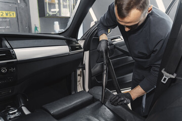 Man cleaning his car with vacuum cleaner. Man in a black uniform.