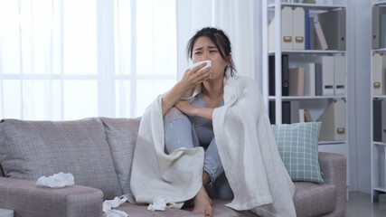 korean woman with infection touching sore throat and head hurts sitting on couch while using warm...