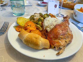 Above view of Thanksgiving dinner. Turkey leg, bread roll, sweet potatotes stuffing and mashed potatoes on a white plate on a tan table cloth.