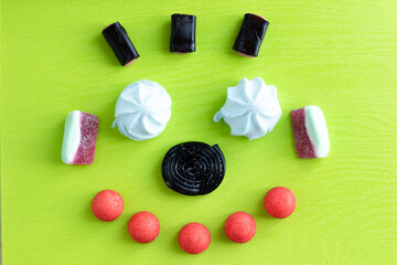Candy teeth sweet smile flat lay colorful fruit marmalade, marshmallow and black licorice candies on green background.