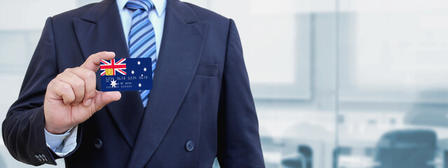 Cropped image of businessman holding plastic credit card with printed flag of Australia. Background blurred.