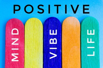 POSITIVE MIND VIBE LIFE text and colorful wooden stick on blue background