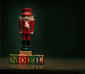 Red vintage nutcracker standing on antique child's blocks that spell the word NOEL