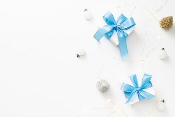 Holiday winter blue. White gift box with blue ribbon, New Year balls in Christmas composition on white background for greeting card. Copy space. Winter holidays, New Year.