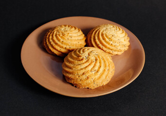 Several shortbread cookies with poppy seeds on a saucer on a black background. A night snack of a sweet tooth.