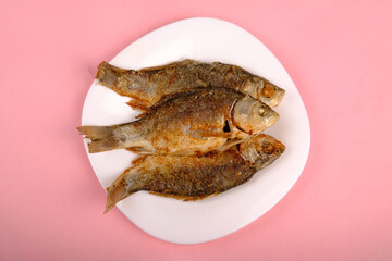 fried crucian carp with golden crust on a white plate on a pink background, cooked fish