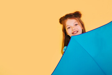 A girl in a blue dress with an umbrella on a yellow background. Child teenager studio photo. Under...