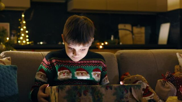 Surprised cute kid boy opening big Christmas present looking inside magic lights shining brightly. Christmas gift. Winter holidays. Children. Emotions concept.