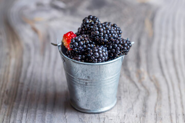 Fresh blackberries in a bucket on a wooden background. Rustic style.