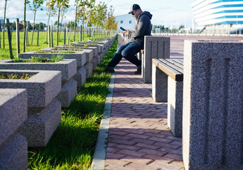 Serious young man texting on the cellphone. Handsome young male is sitting on a park bench and...