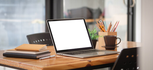 Close up view of simple workplace with laptop computer, notebook, coffee cup and stationery on wooden table.