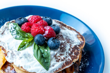 Pancakes with blueberries and raspberries with white sauce and Basil leaf. A sweet Breakfast