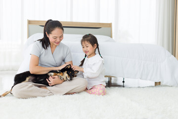 Adorable Asian mother and daughter hold a puppy in bedroom.