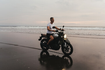 Obraz na płótnie Canvas Surfer rides on motorbike with surfboard at sunset ocean beach. Bali island, Indonesia