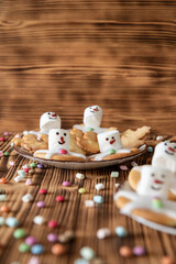 Plätzchen mit Marshmallows, Zuckerguss und Schokolinsen die aussehen wie geschmolzene Schneemänner auf Tellern zur Weihnachtszeit
