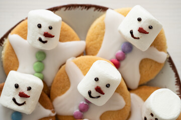 Plätzchen mit Marshmallows, Zuckerguss und Schokolinsen die aussehen wie geschmolzene Schneemänner auf Tellern zur Weihnachtszeit