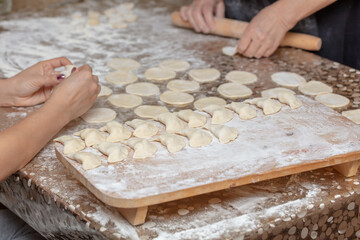 A girl and a woman make dumplings from dough.
