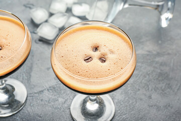 Two glasses of tasty espresso martini cocktail and ice cubes on table
