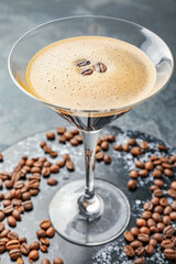 Glass of tasty espresso martini cocktail and coffee beans on table