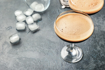 Two glasses of tasty espresso martini cocktail and ice cubes on table