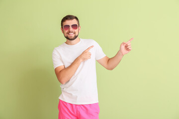 Handsome man with stylish sunglasses showing something on color background