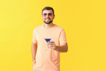 Handsome man with stylish sunglasses and cocktail on color background