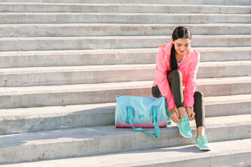 Sporty young woman tying shoelaces outdoors