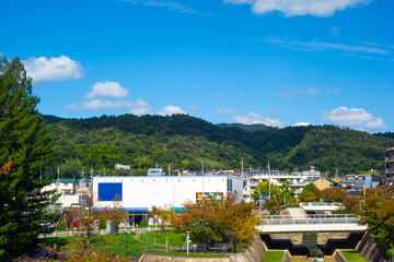 青空に浮かぶ白い雲と山の麓にある建物と道路に架かる橋のある風景