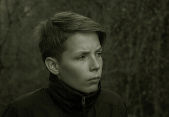 Dramatic black and white close-up portrait of a teenager in nature. Close-up of a worried depressive boy's face against a blurred background of trees.High quality photo