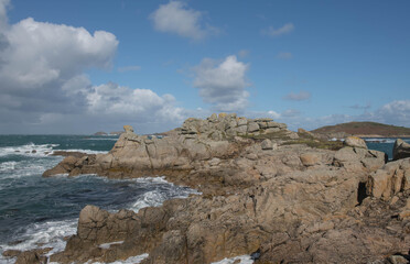 Granite Boulders on the Coast with a Cloudy Blue Sky and Rough Sea Background on the Island of Bryher in the Isles of Scilly, England, UK