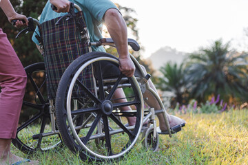 Rear view of disabled handicapped man in wheelchair and care helper walking in park.