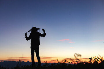 Silhouette of young girl standing lonely on mountain at beautiful sunset