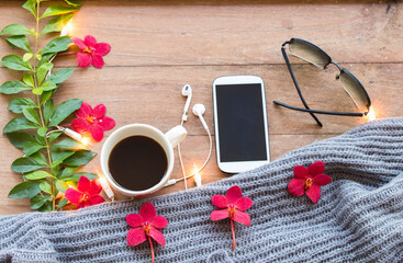 mobile phone ,hot coffee ,sunglasses and knitting wool scarf of lifestyle woman relax in winter season with red orchid ,decorate light background wooden