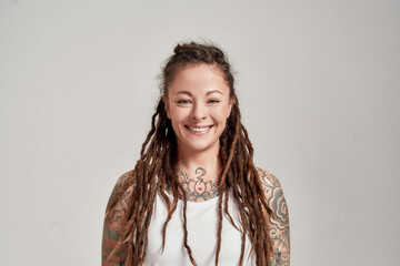 Portrait of young tattooed caucasian woman with dreadlocks wearing white shirt, smiling at camera...